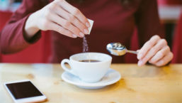 Person Pouring Sugar into Coffee Cup