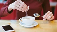 Person Pouring Sugar into Coffee Cup