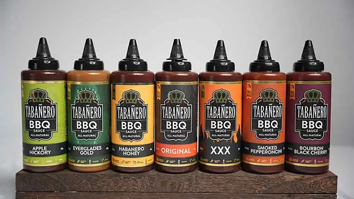 Assortment of barbecue sauces in multiple flavors, including apple hickory, habanero honey, smoked pepperoncini, and bourbon black cherry, displayed in squeeze bottles.