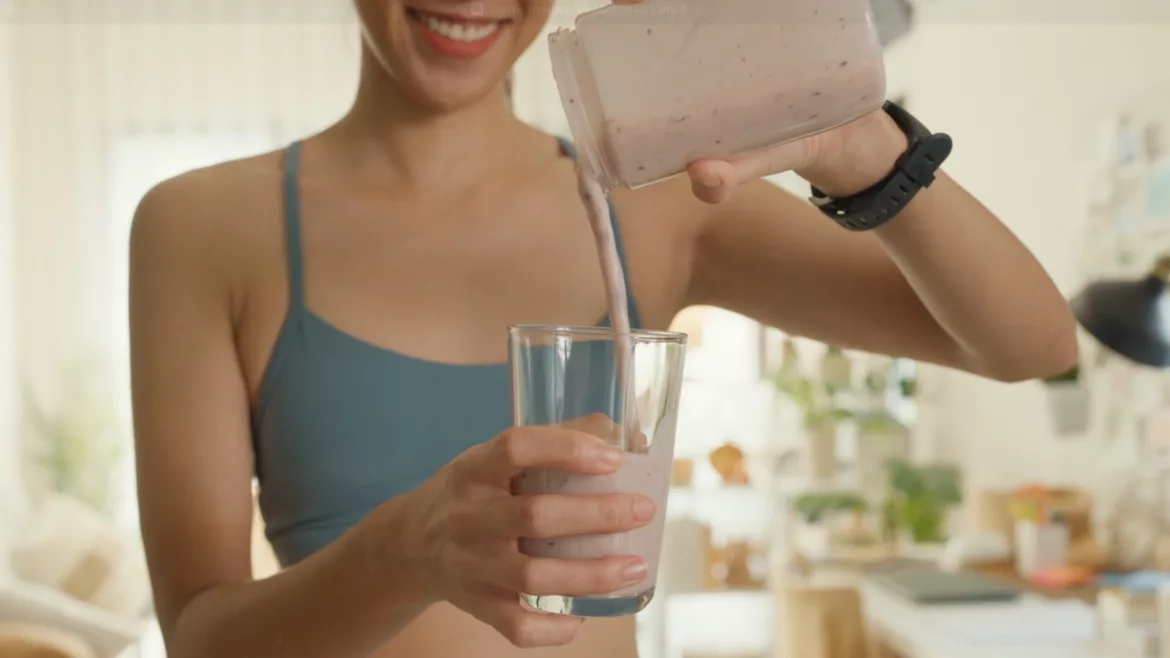 Cropped image of smiling young woman in a sports bra pouring herself a protein drink.
