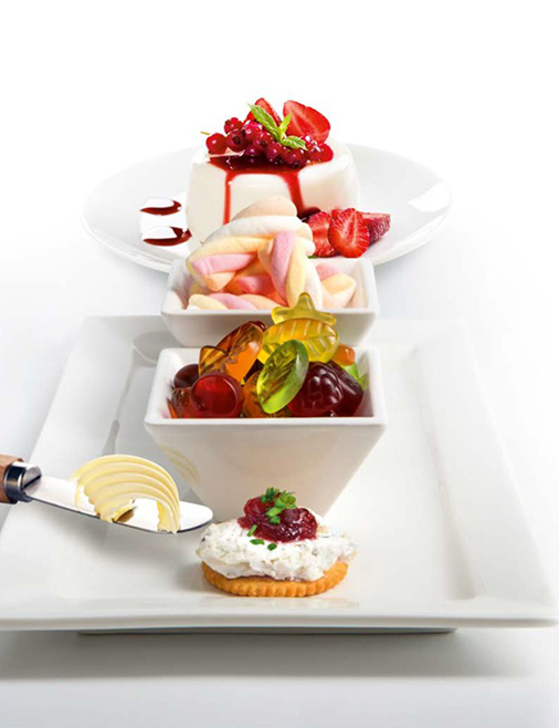 A row of desserts and candy in white bowls, a cracker with cream and fruit, and a butter knife with butter.