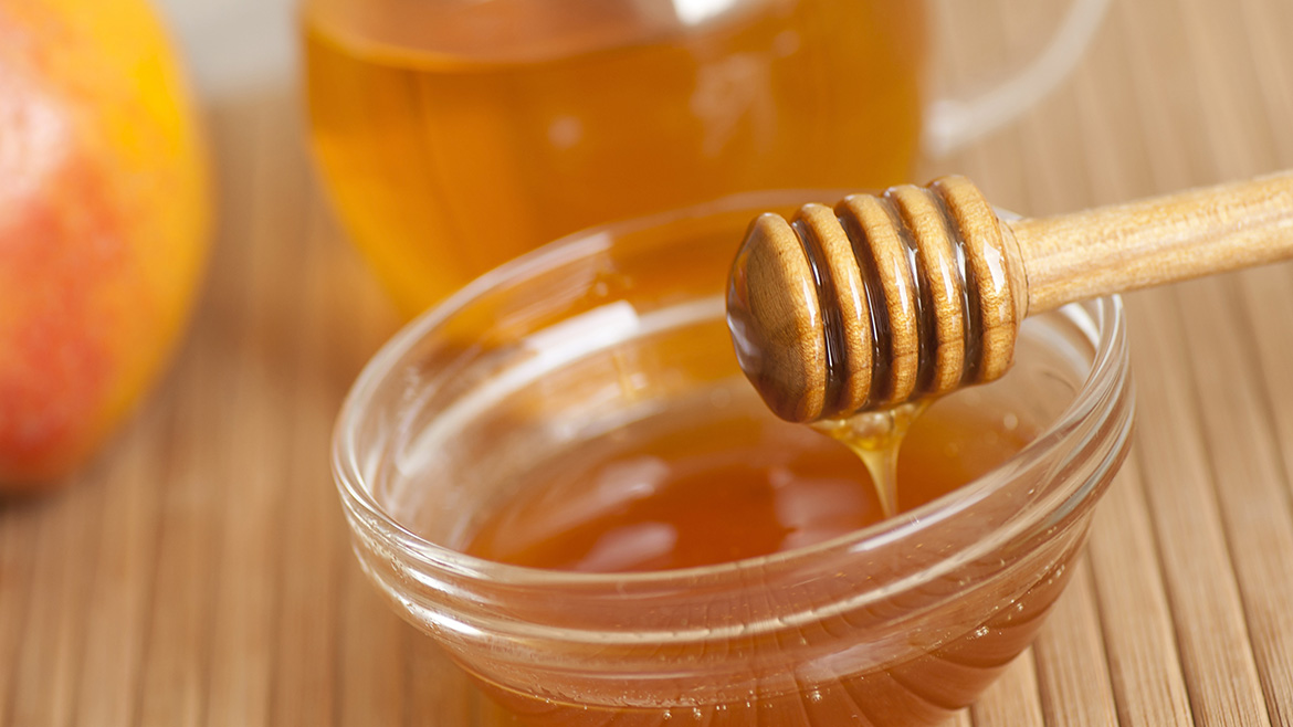 Close up of a small bowl of honey and a honey dipper.