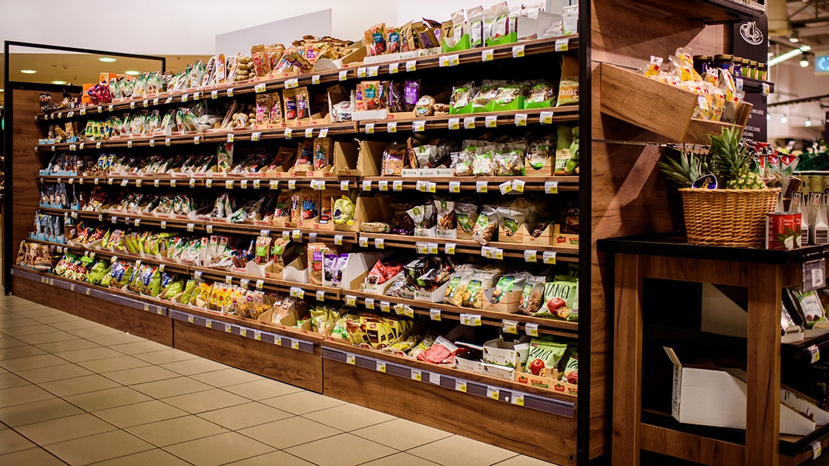 Supermarket asile with long shelves of packaged snack and goods, and a side display with pinapples.