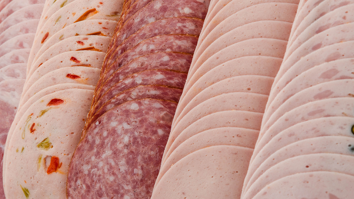 Close-up of rows of various sliced deli meats including ham, salami, and peppered turkey.