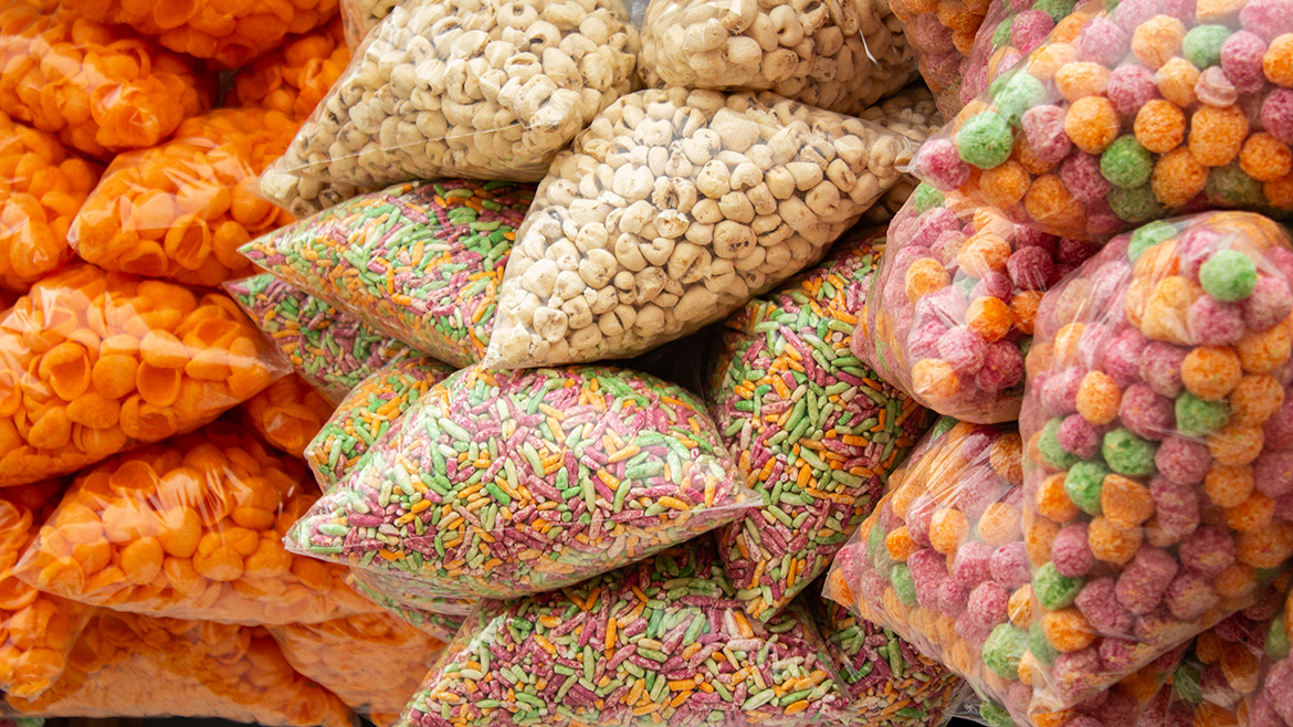 Bags of assorted, colorful Indian snacks: orange shells, white puffs, sprinkles, and colorful puffballs.