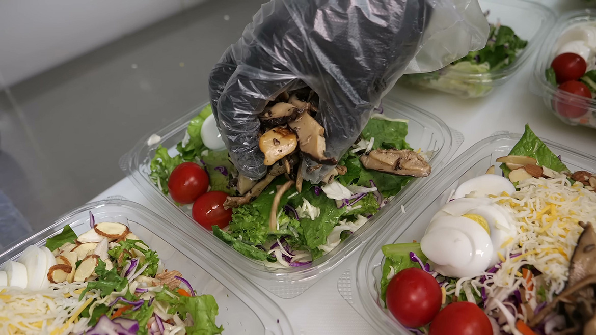 Gloved hand packaging prepared salads in containers.