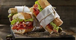 Deli sub sandwiches cut in half and wrapped in white paper and natural rope.