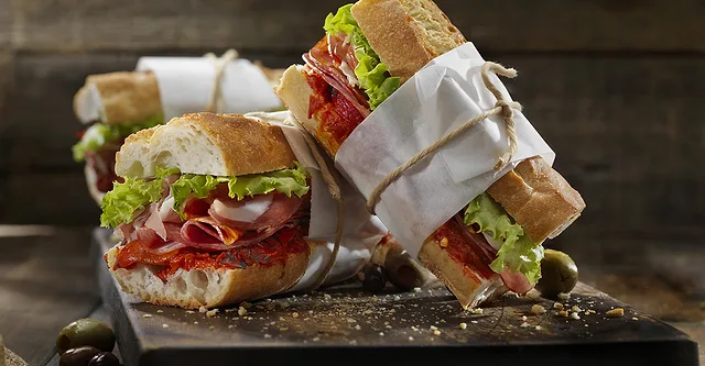 Deli sub sandwiches cut in half and wrapped in white paper and natural rope.