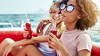 Two women on a boat, drinking bottles sodas with straws.