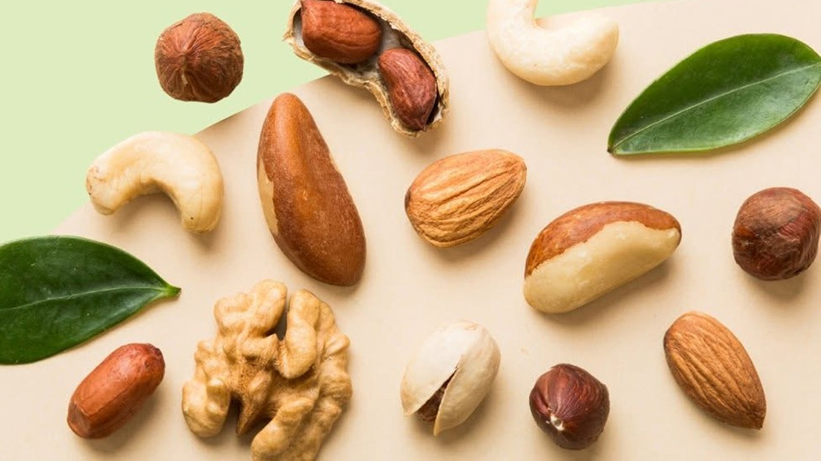 Various unshelled and shelled nuts and two green leaves spread on a white and green background.