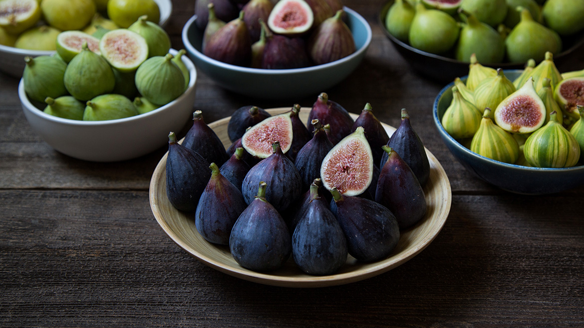 Several different types of bowls full of whole and sliced figs in different shades of green and purple.