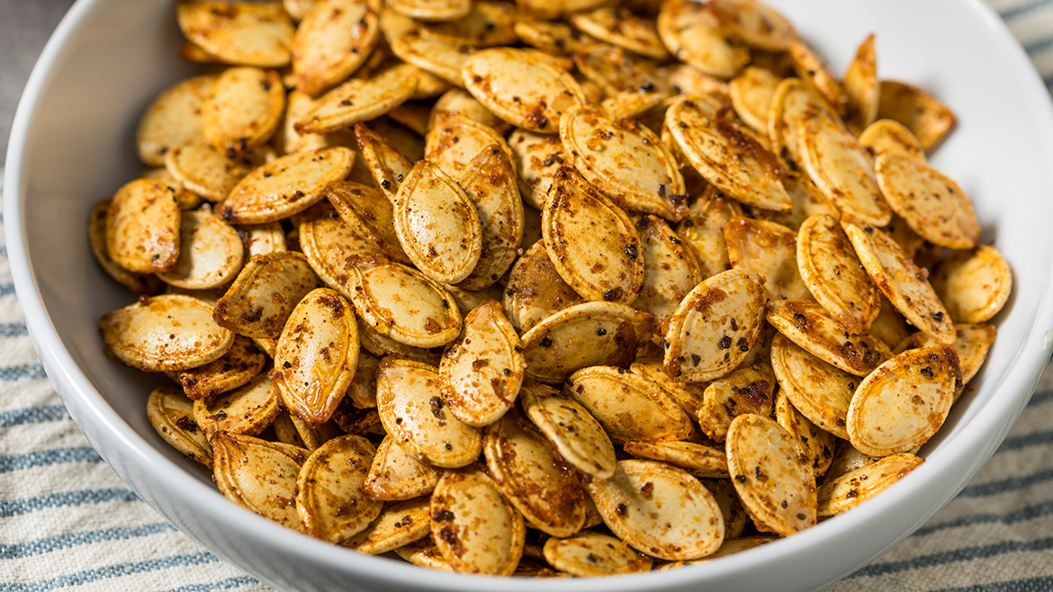 A white bowl full of seasoned pumpkin seeds.