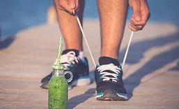 Person Tying Shoes Next to Green Health Drink