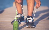 Person Tying Shoes Next to Green Health Drink